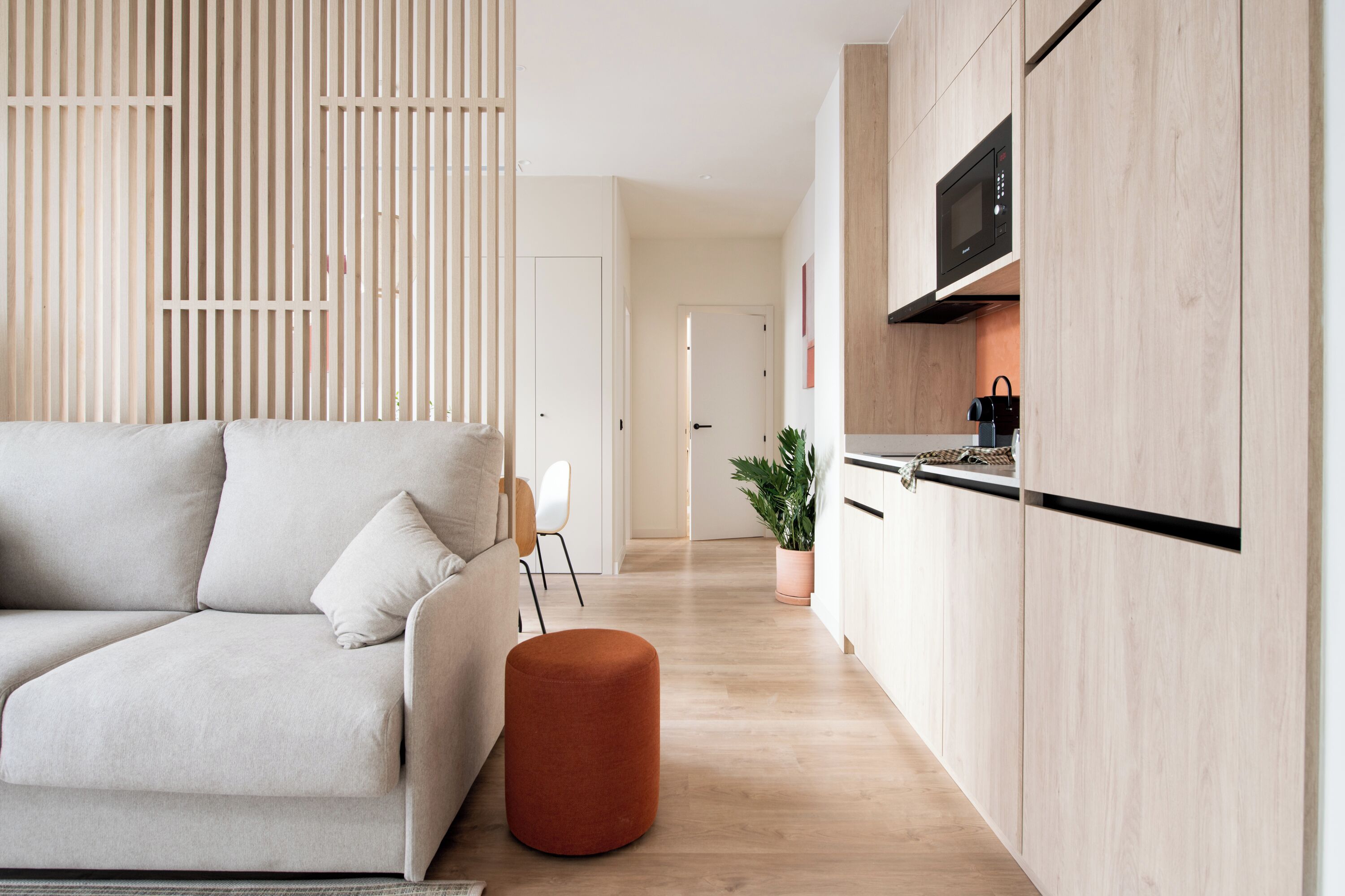 A modern living room with a sofa, ottoman, and a wooden partition.