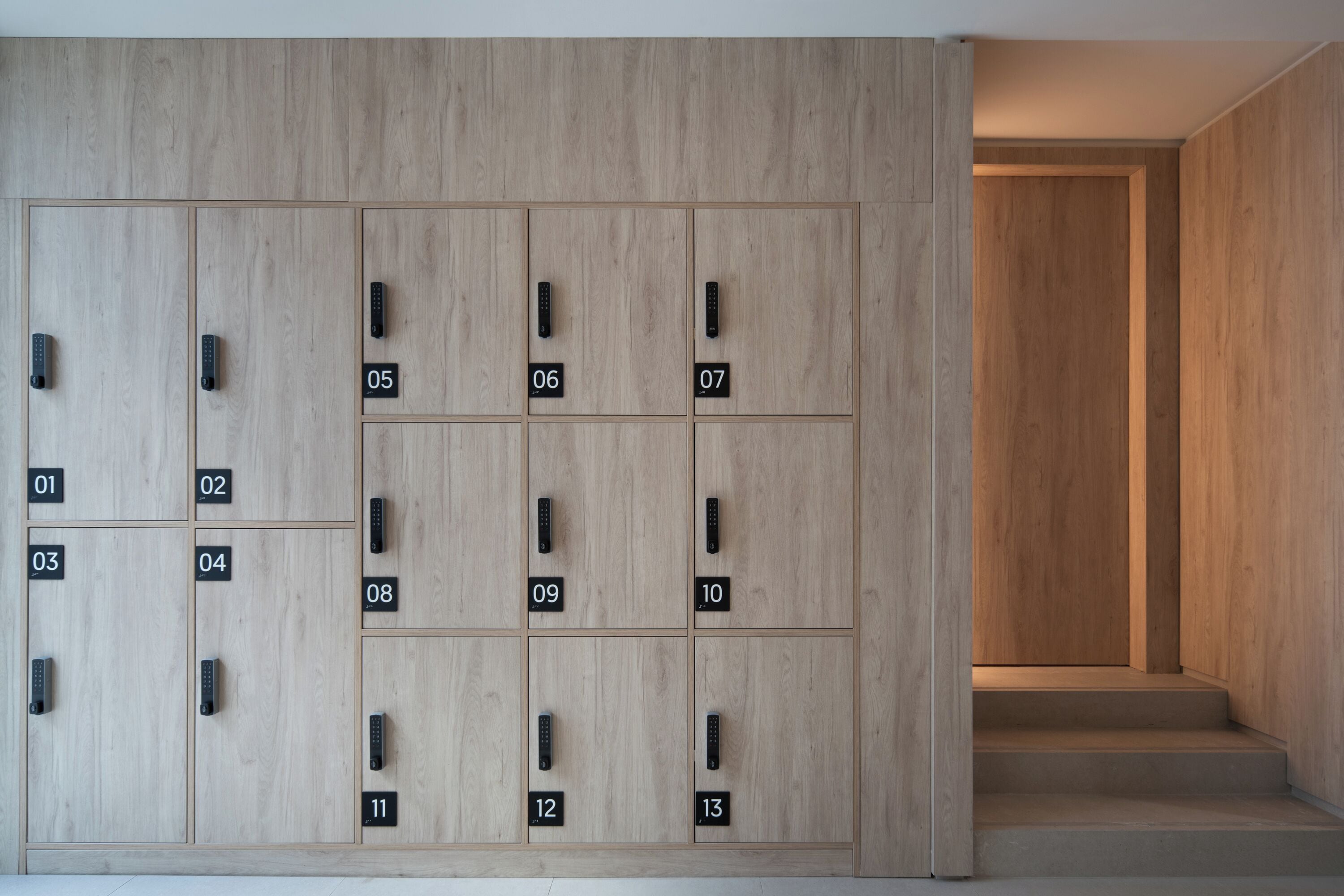 A row of wooden lockers numbered 01 to 13, with a staircase leading to a door on the right.