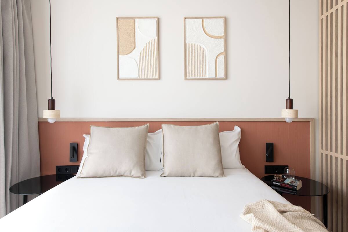 A hotel room with a bed, two bedside tables, a nightstand, and two wall-mounted light fixtures.