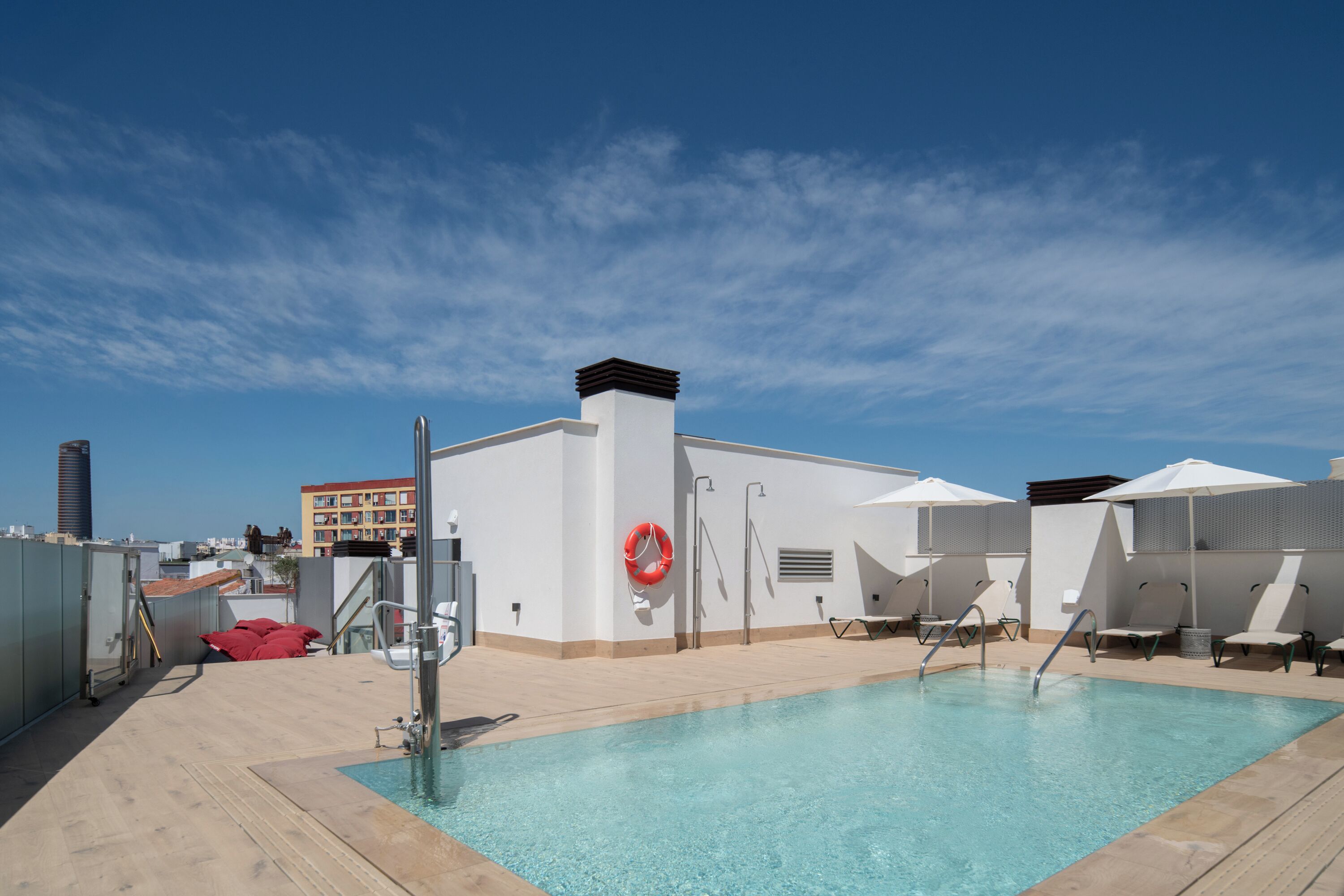 A rooftop pool with clear blue water, a lifebuoy, and lounge chairs.
