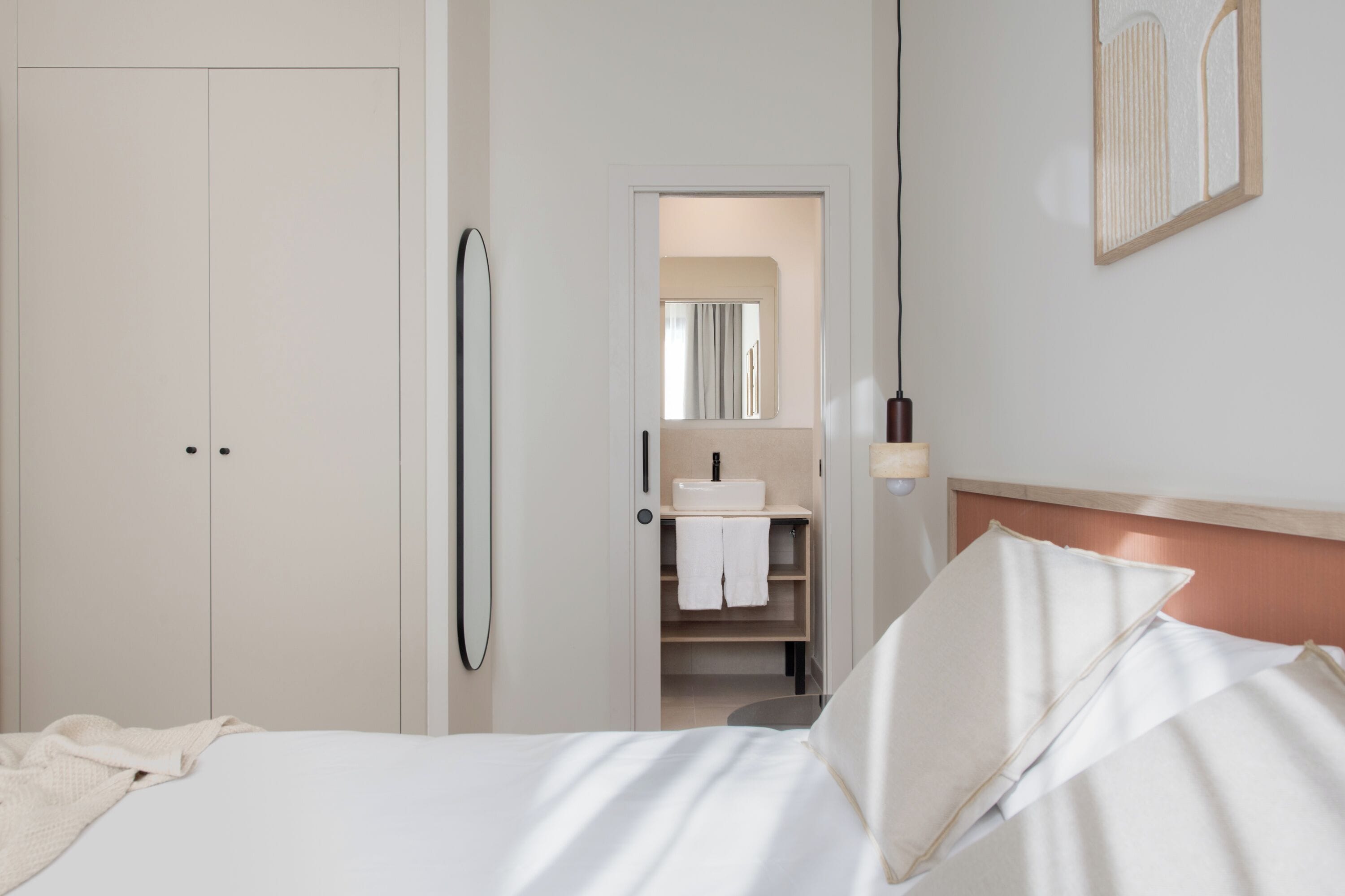 Ein Schlafzimmer mit Bett, Kleiderschrank, Spiegel und einem durchgehenden Türspalte sichtbaren Badezimmer.