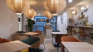 A modern interior with wooden tables and chairs, pendant lighting, and a kitchen area in the background. - Líbere Seville Plaza Nueva (Seville)