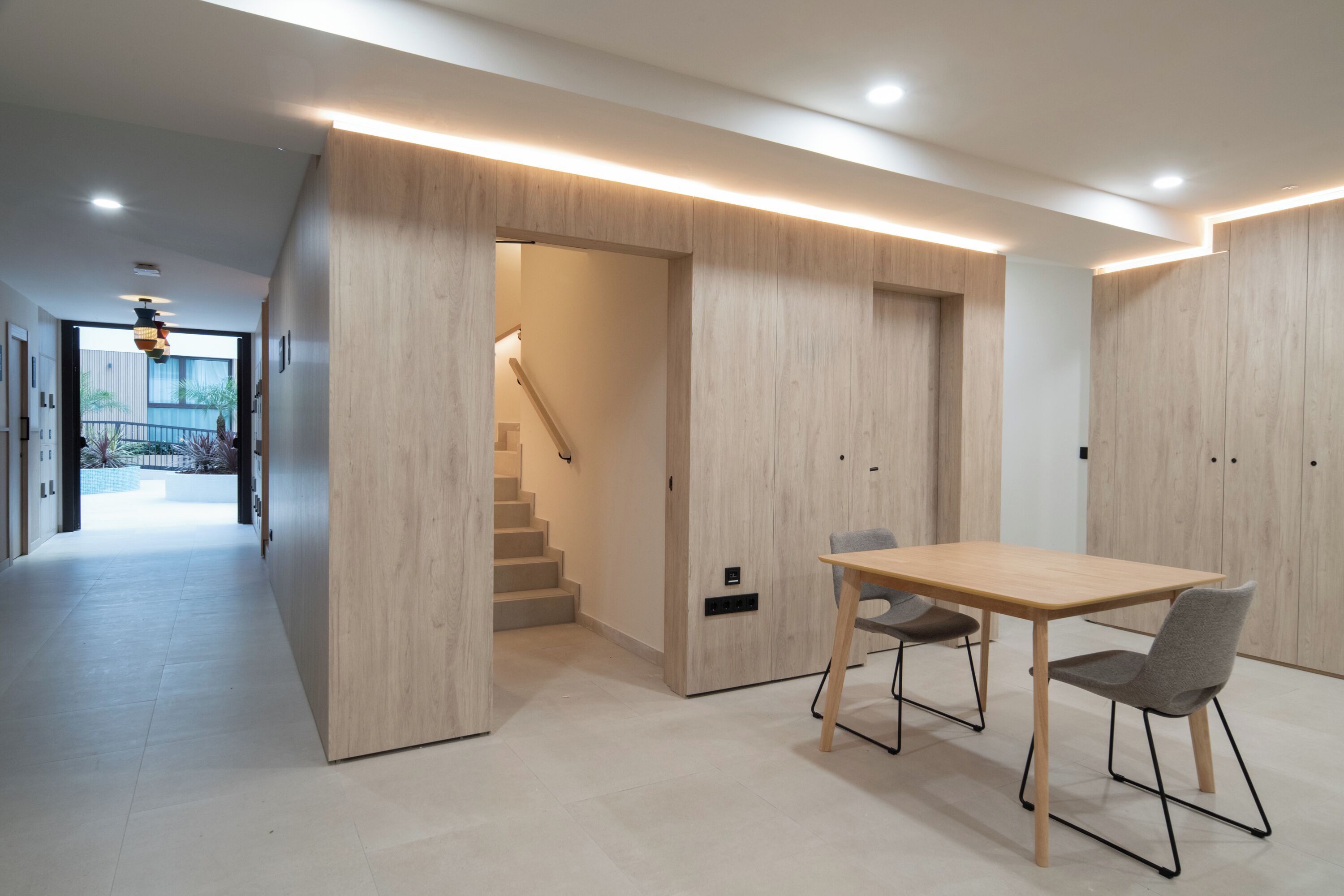Un interior moderno con una pared de acento de madera, una escalera y un comedor con mesa y sillas.