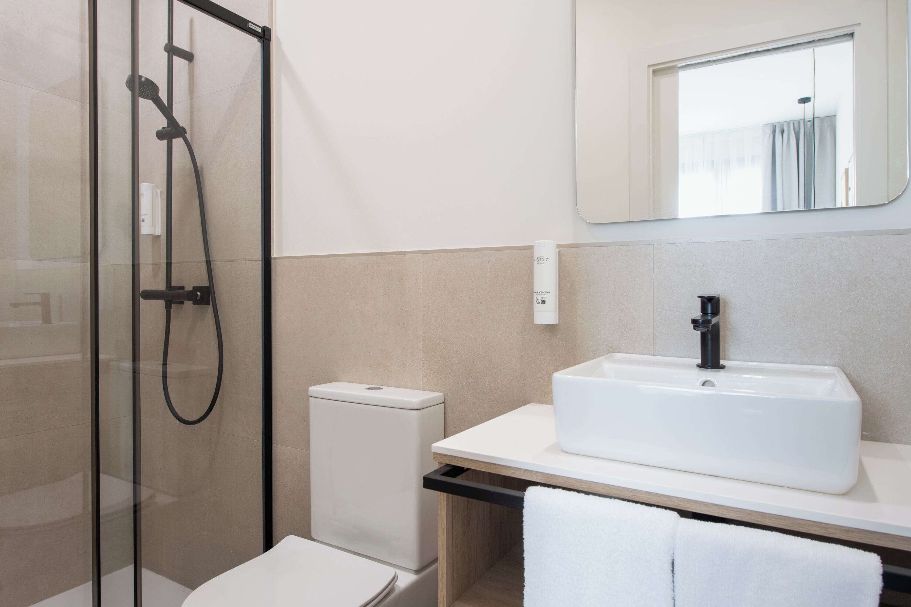 Un baño moderno con ducha envuelta en vidrio, un lavamanos blanco y un espejo sobre él.