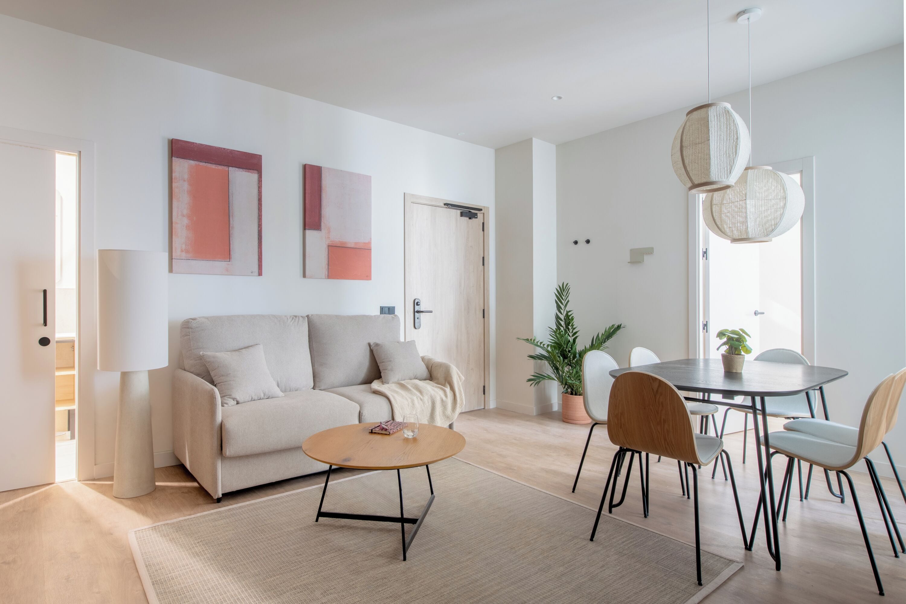 Un salon moderne avec un canapé, une table basse et une table à manger avec des chaises. On peut y admirer des tableaux abstraits au mur, une plante en pot et un luminaire suspendu.