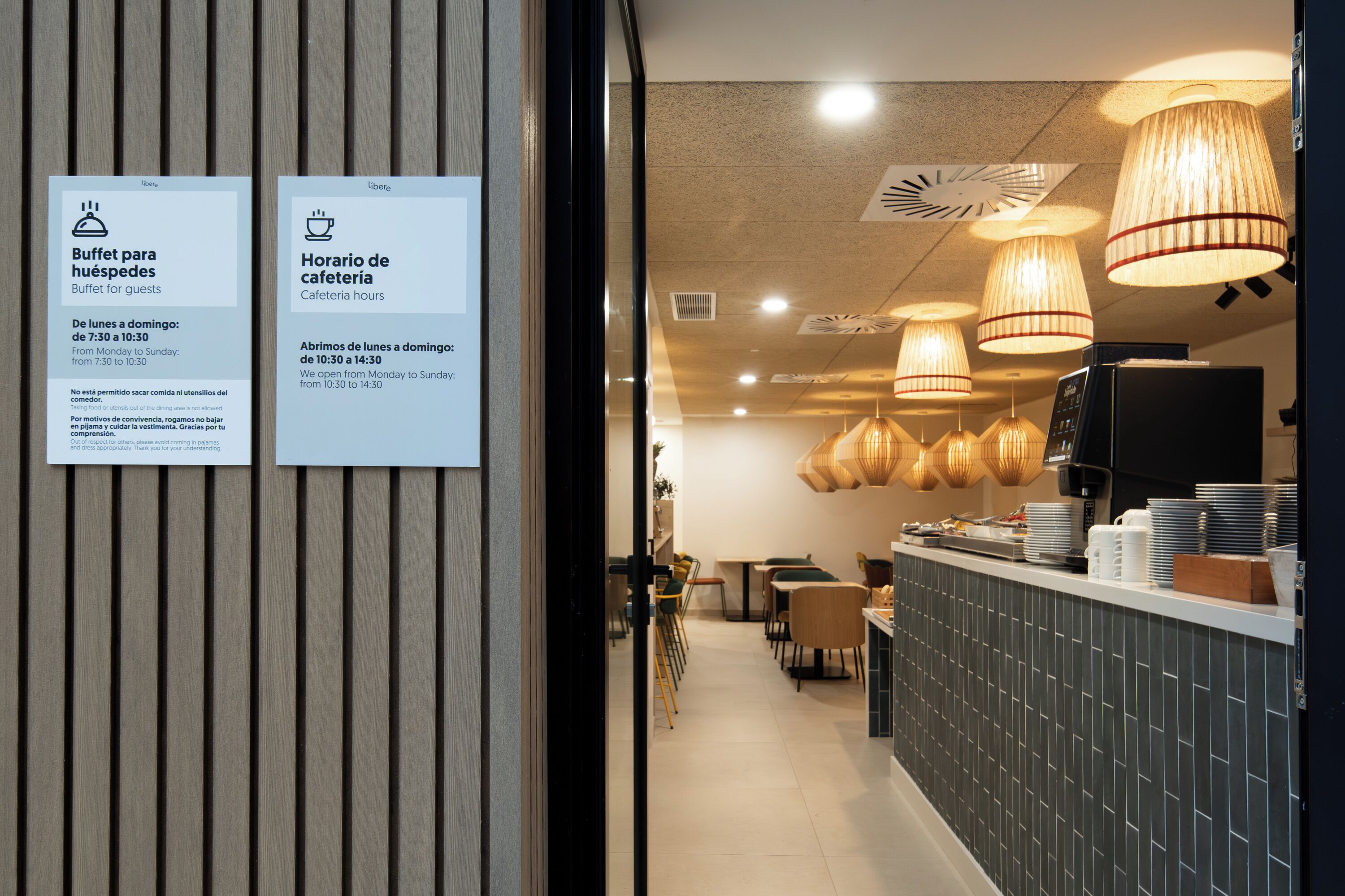 Un intérieur moderne comprenant un espace buffet, un café et un comptoir où sont empilées des assiettes et des tasses.