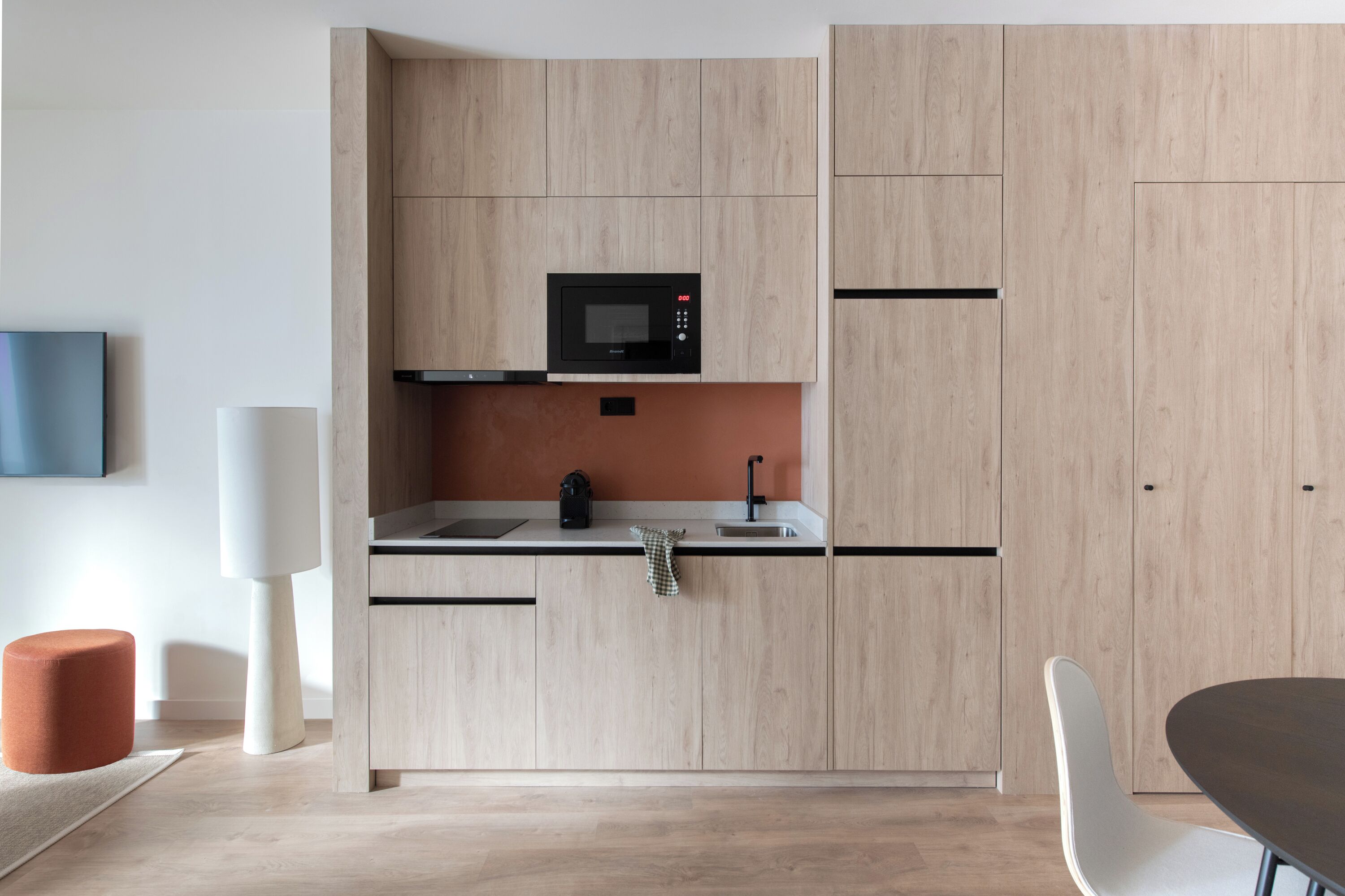 A modern kitchen with light wood cabinetry, a black microwave, and a stainless steel sink.
