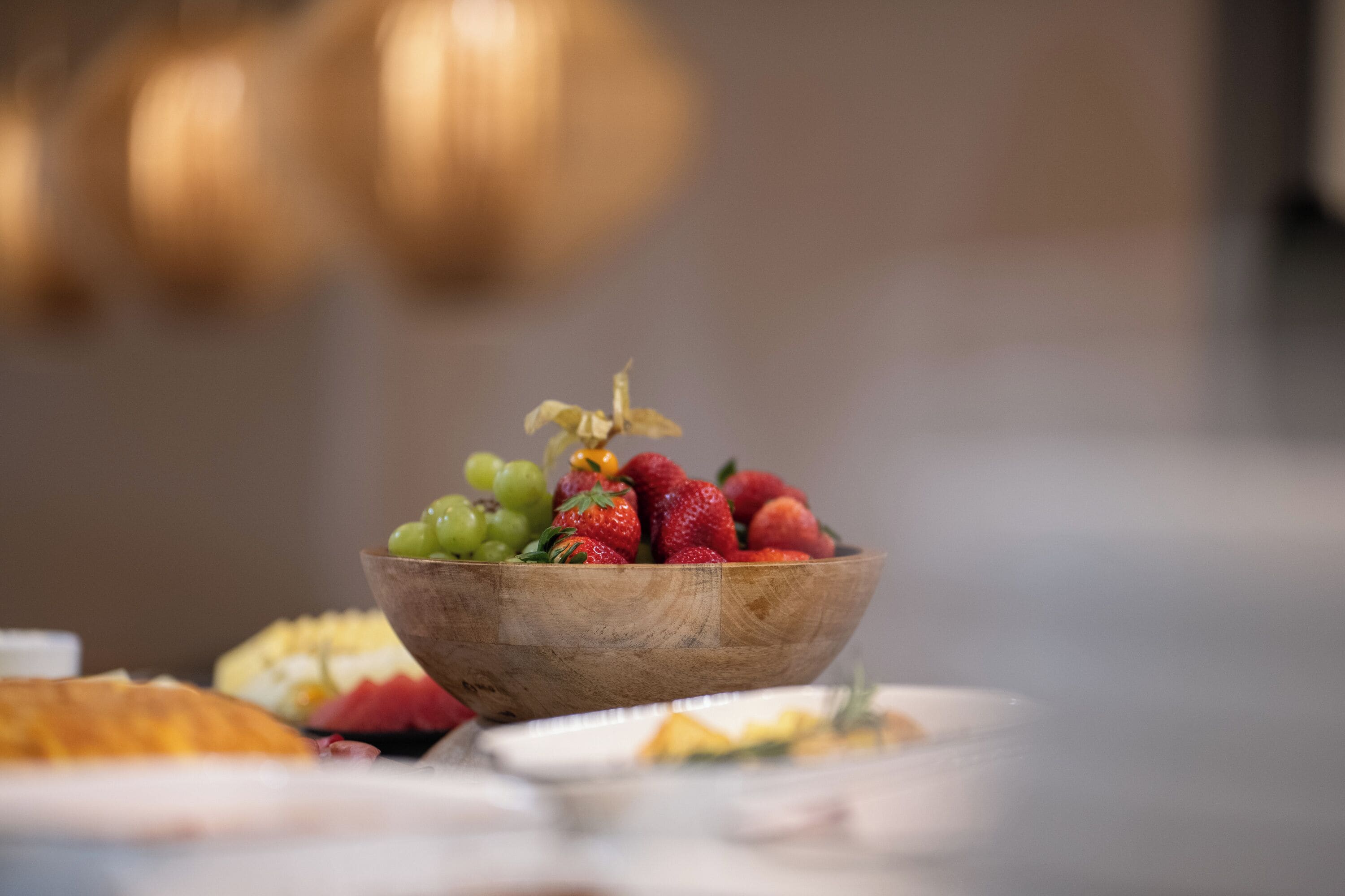 Un cuenco de madera lleno de fresas y uvas sobre una mesa.