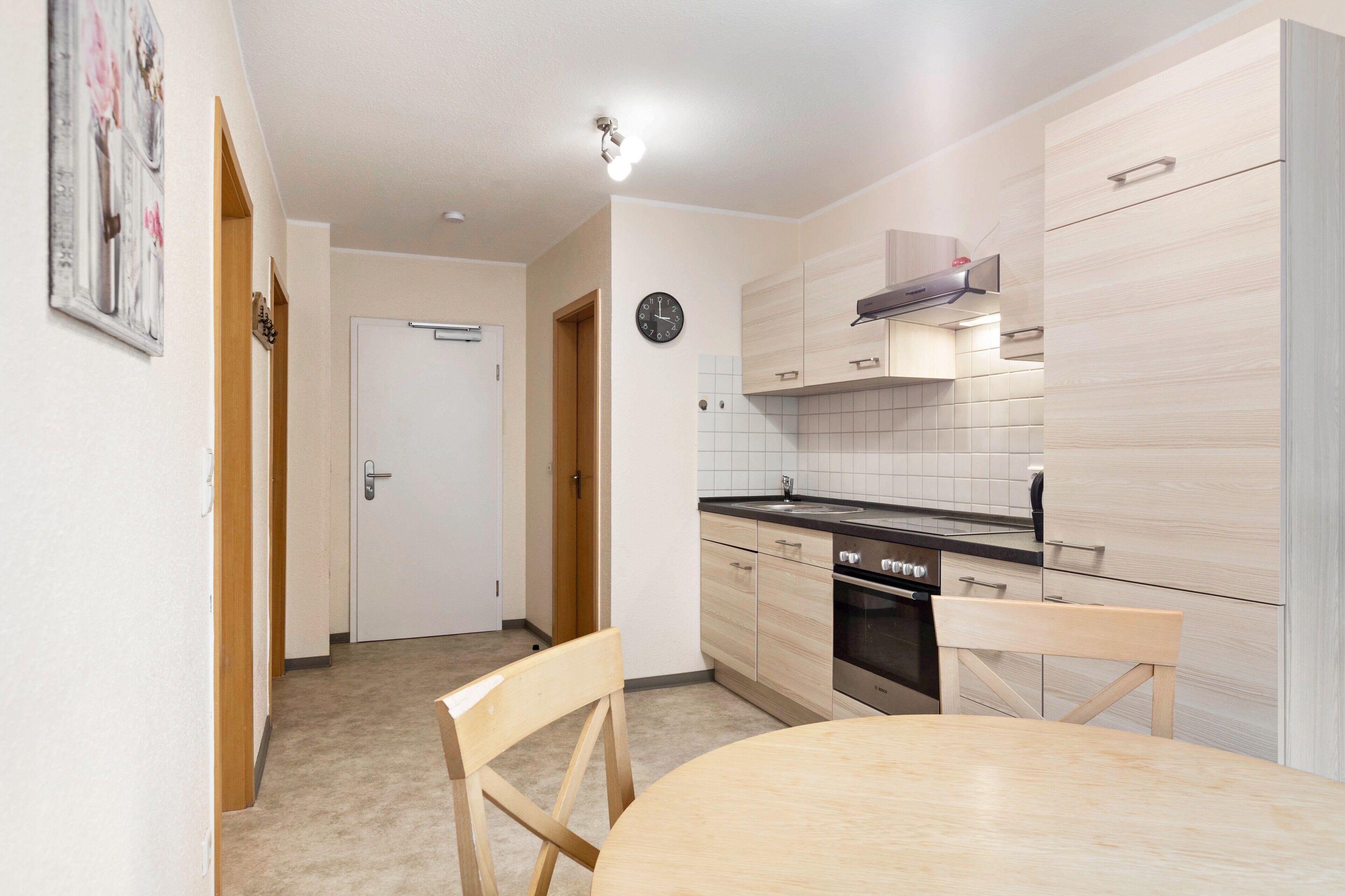 Una cocina compacta con una mesa de comedor, sillas, un reloj y una puerta que da a otra habitación.