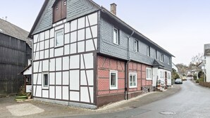 Ein traditionelles Fachwerkhäuschen mit einem steilen Satteldach, einem Schornstein und einer kleinen Veranda.