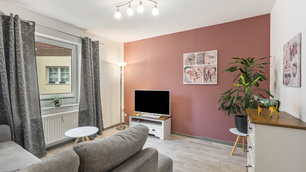 Ein modernes Wohnzimmer mit einer Couch, einem Fernseher, einem kleinen Tisch und einer Pflanze.
