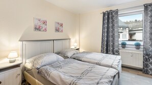 Ein Schlafzimmer mit Bett, Nachttischen, einem Fenster mit Vorhängen und Wanddekorationen.