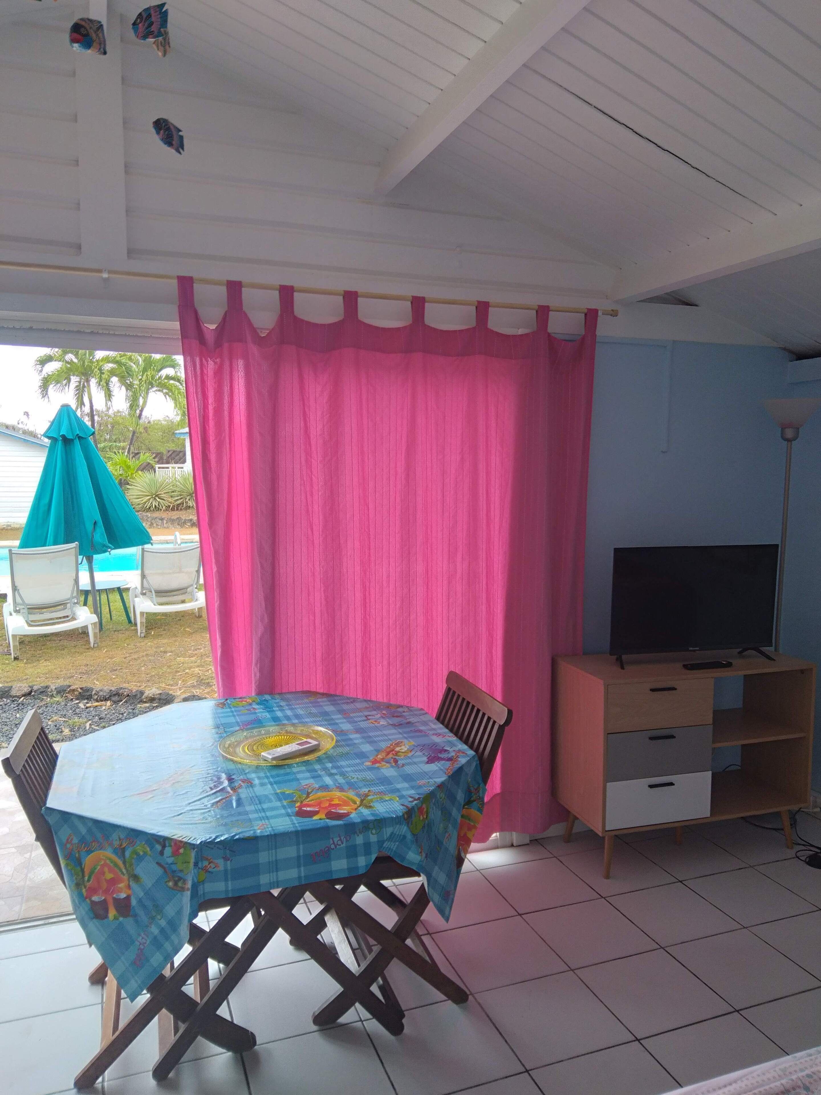 A covered patio area with a table and chairs, a television, and a pink curtain.