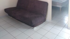 A room with a dark brown sofa, a framed picture on the wall, and a bed in the adjacent room. - les gîtes hoprins (Le Moule)