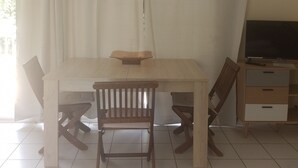 A room with a wooden table, two chairs, a TV, and a ceiling fan. - les gîtes hoprins (Le Moule)