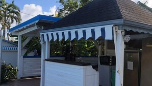 A small outdoor kiosk with a blue and white striped awning, a tiled floor, and a metal roof. - les gîtes hoprins (Le Moule)