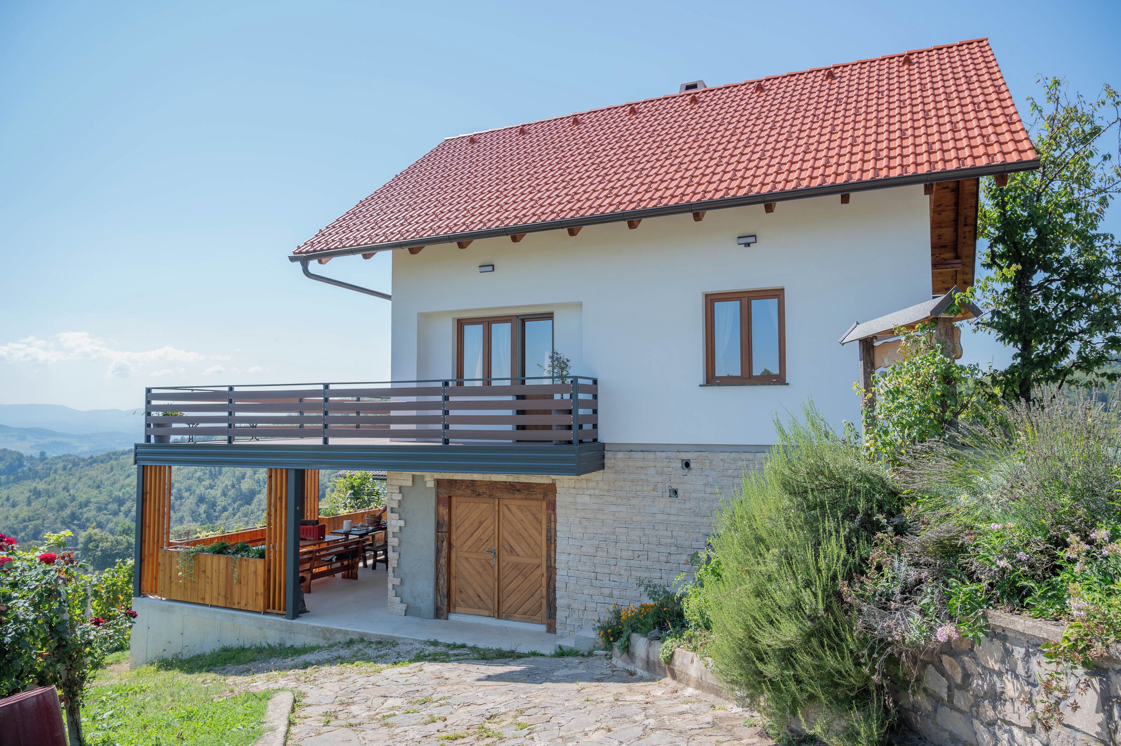 Une maison à deux étages, avec un toit recouvert de tuiles rouges, un balcon et un mur en pierre.