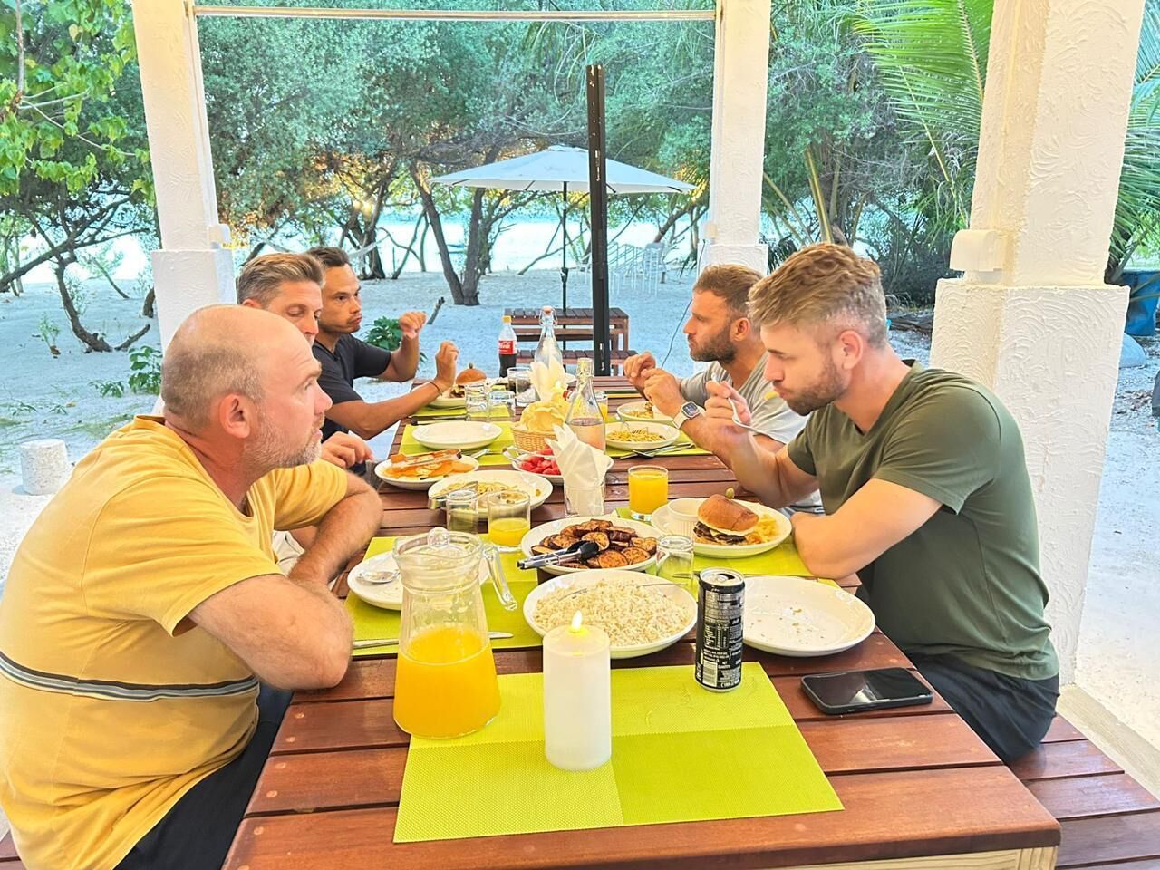 Un grupo de personas cenando en una mesa al aire libre, con varios platos, bebidas y una vela.