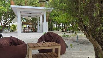 An outdoor seating area with a wooden table and two bean bags, surrounded by trees and a white structure in the background.