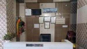 A reception area with a tiled wall, a reception desk, and a black office chair. - Hotel Sharma Guest House  (Naina Devi)