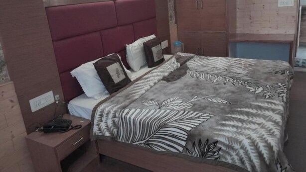 A bedroom with a large bed, a nightstand, a wardrobe, and a patterned bedspread. - Hotel Sharma Guest House  (Naina Devi)
