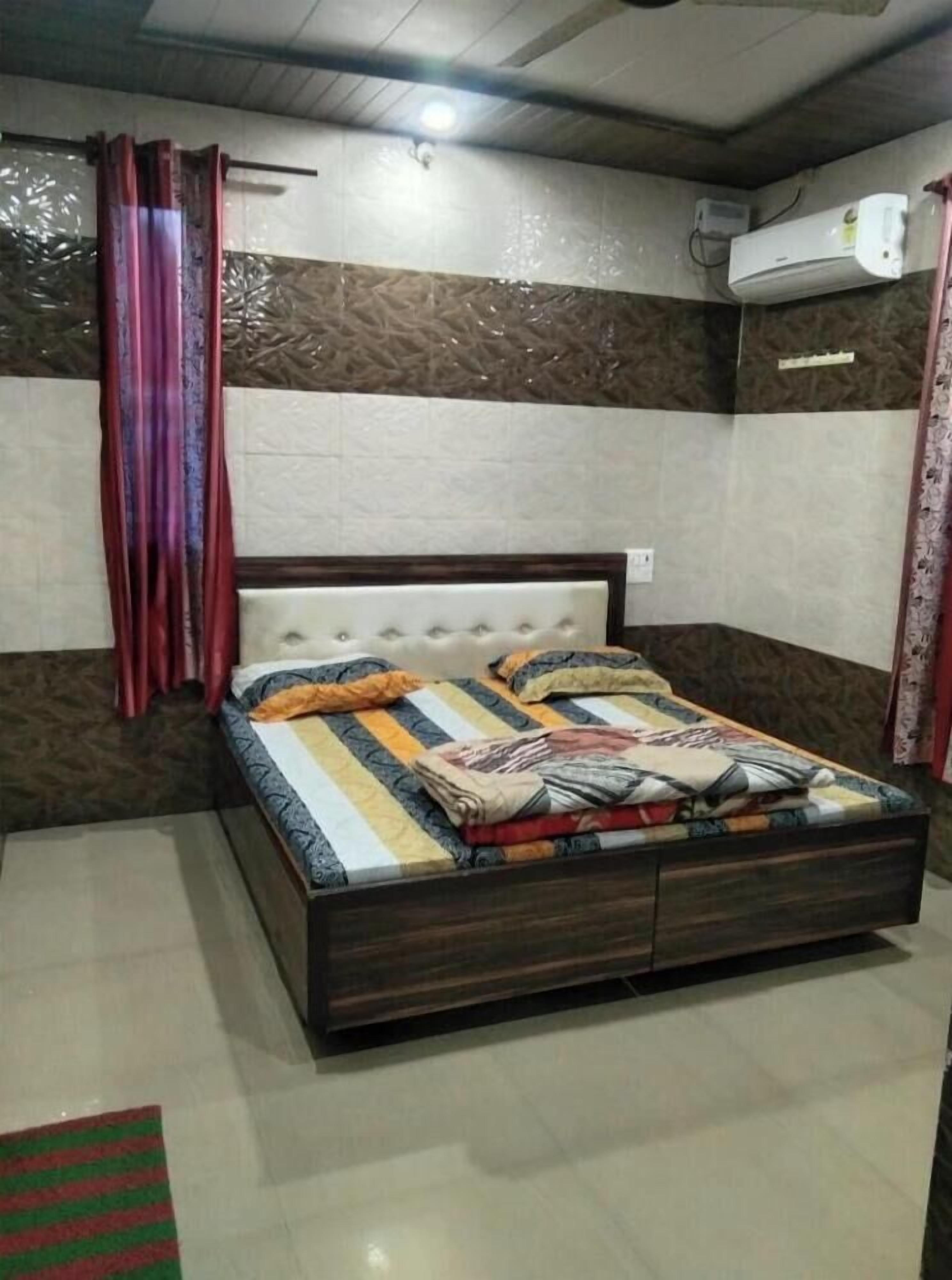 A bedroom with a bed, curtains, an air conditioning unit, and a patterned wall.