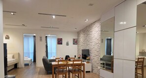 Ein modernes Wohnzimmer mit Essbereich, einer Couch, einem Fernseher und einer Steinwand.