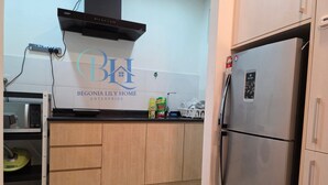 Una cocina con gabinetes de madera, un refrigerador de acero inoxidable y un microondas. Hay un letrero en la pared que dice "BEGONIA LILY HOME ENTERPRISE".