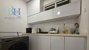 Una cocina moderna con armarios blancos, microondas, cafetera y escurreplatos.