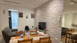 Una sala de estar moderna con comedor, un televisor de pantalla plana montado en una pared texturizada y una mesita auxiliar con una planta.