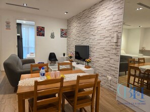 Ein modernes Wohnzimmer mit Essbereich, einem flachbildfernseher an einer strukturierten Wand und einem kleinen Beistelltisch mit einer Pflanze.