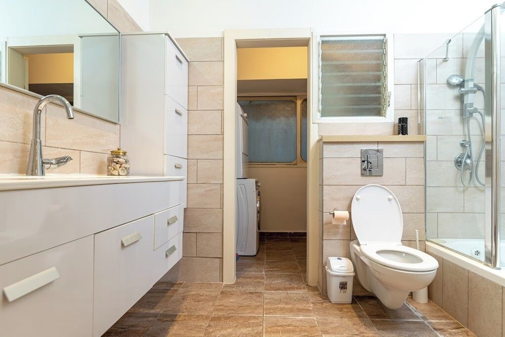 A modern bathroom with a sink, mirror, toilet, shower, and a small window.