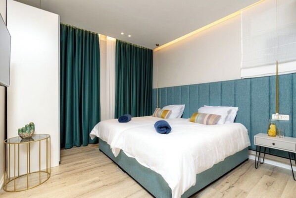 A modern hotel room with a large bed, teal curtains, a white headboard, and a small bedside table with a lamp. - Luxury apartment with panoramic view (Tiberias)