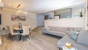 Uma sala de estar moderna com área de jantar, um sofá cinza e uma cozinha com um espelho grande.