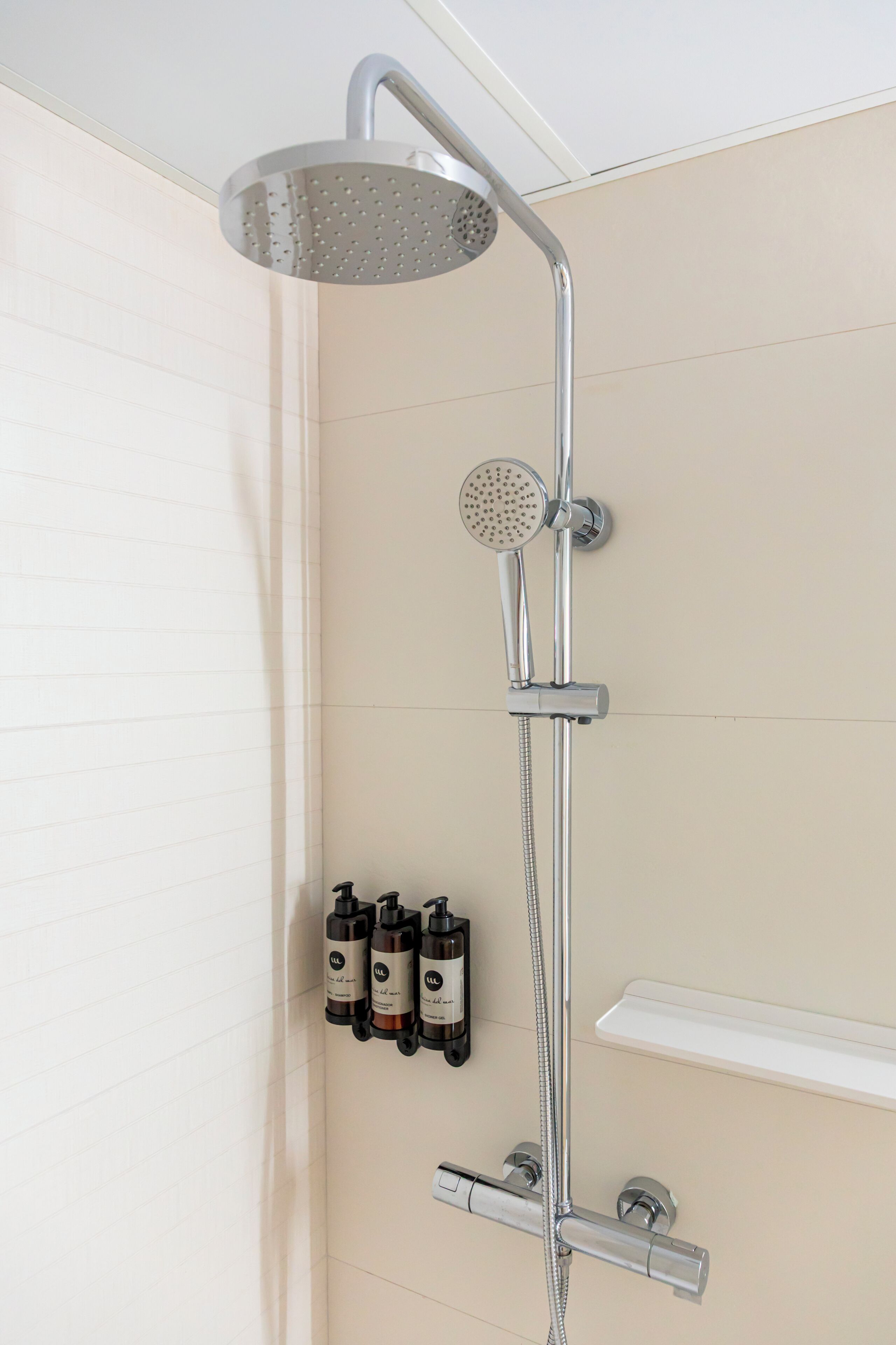Una ducha moderna con cabezal de ducha manual y otro de lluvia fijo, instalada en una pared con revestimiento de azulejos color beige.