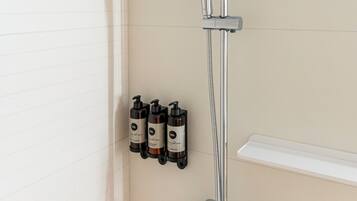 Una ducha moderna con cabezal de ducha manual y otro de lluvia fijo, instalada en una pared con revestimiento de azulejos color beige.