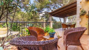 Eine Terrasse im Freien mit Korbmöbeln, Topfpflanzen und einer Pergola.