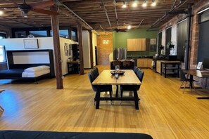 A spacious room with a wooden dining table, a sofa, and a kitchen area with cabinets and appliances. - Brick City Loft (Newark)