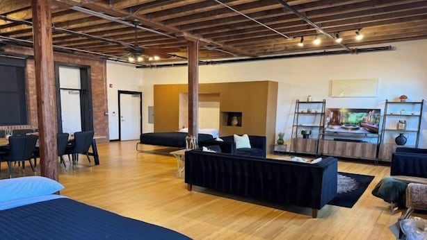 A spacious room with a wooden floor, a black sofa, a bed, and a dining area with chairs. - Brick City Loft (Newark)