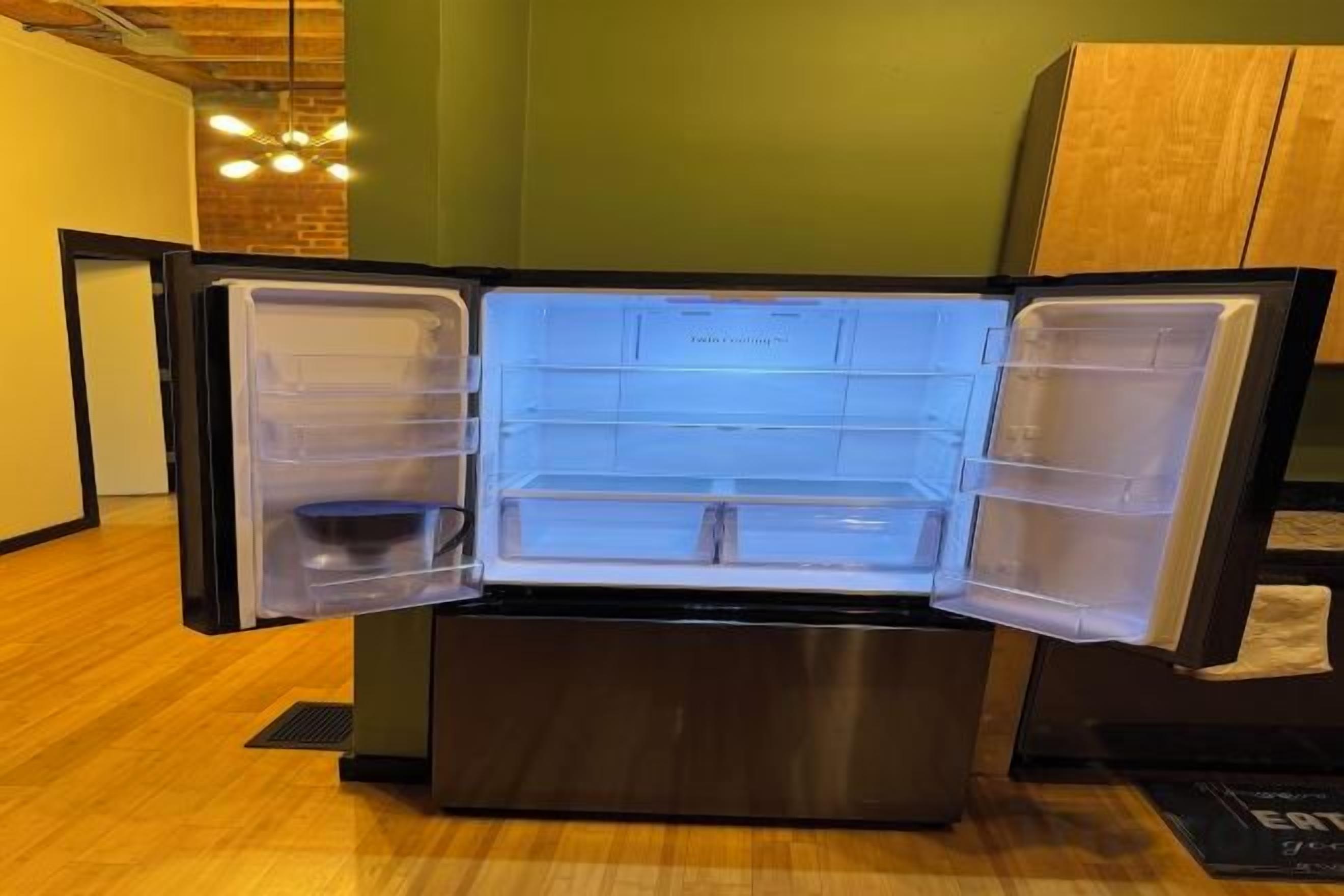 An open refrigerator with multiple compartments, a wooden floor, and a green wall in the background.