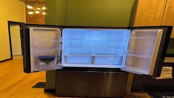 An open refrigerator with multiple compartments, a wooden floor, and a green wall in the background.