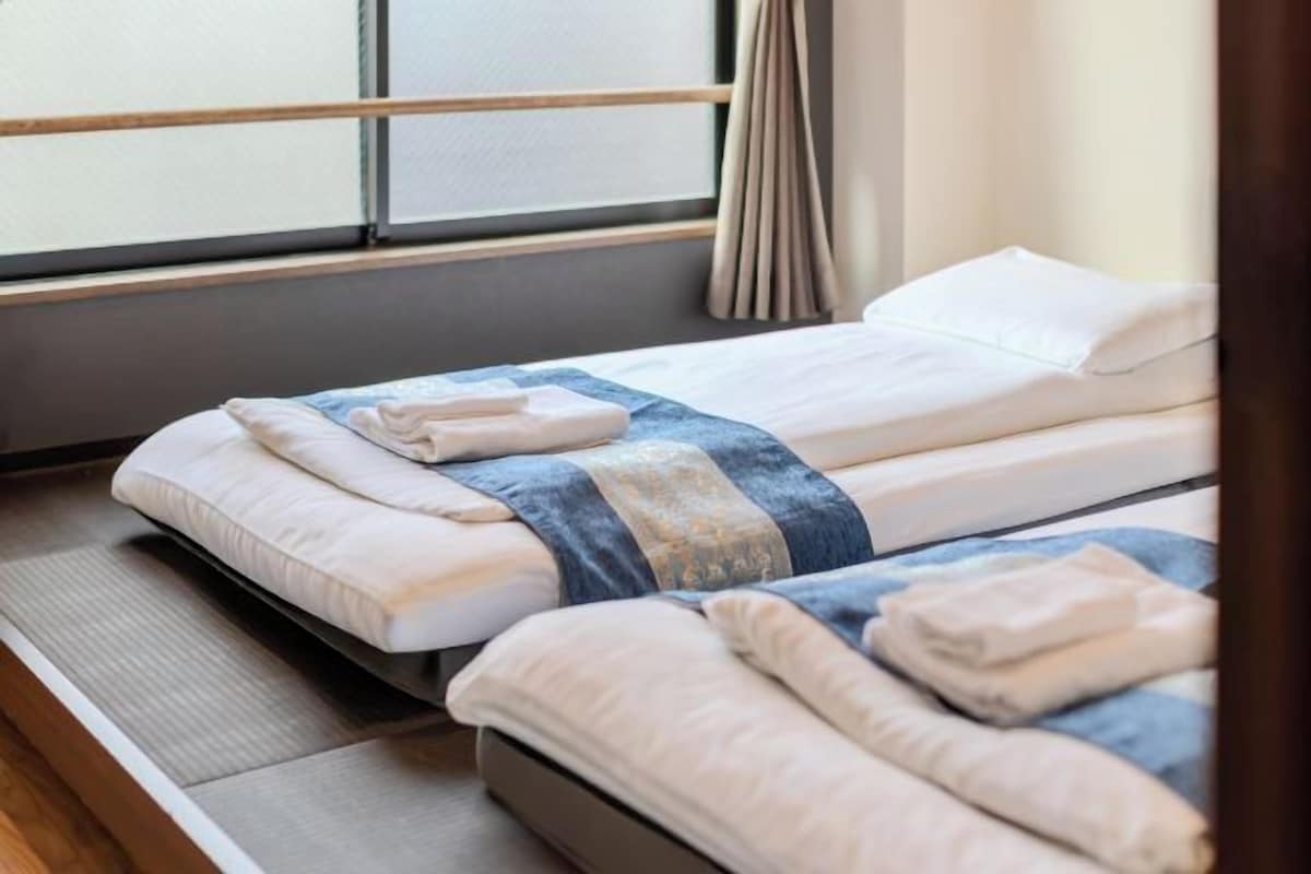 A hotel room with two beds, each with a neatly folded towel and a blanket.