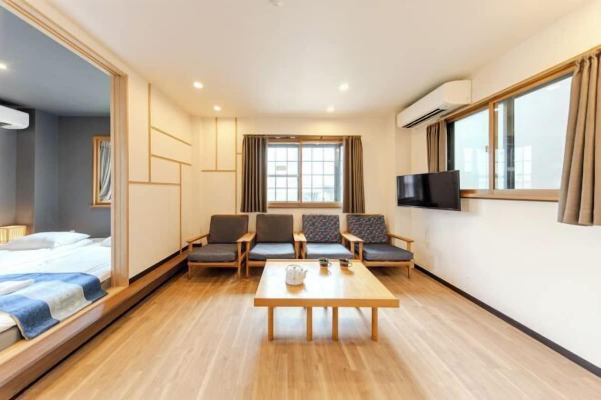 A hotel room with a bed, seating area, TV, and a window.