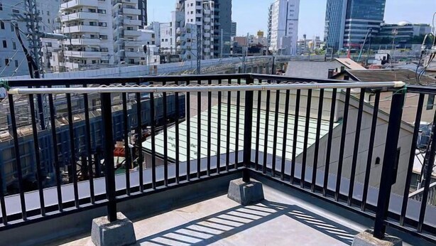 A rooftop terrace with a black metal railing, concrete blocks, and a view of surrounding buildings. - OHAYO・Oshiage (Tokyo)