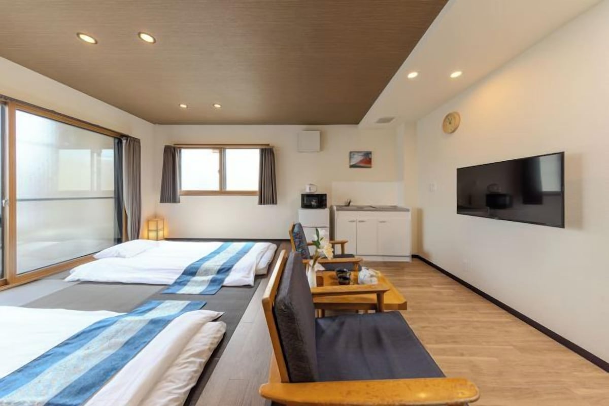 A hotel room with two beds, a sofa, a TV, a kitchen area, and a large window.