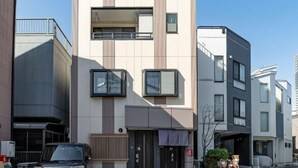 A modern multi-story residential building with a minimalist design, featuring a central entrance with a dark door and windows on the upper floors. - OHAYO・Oshiage (Tokyo)