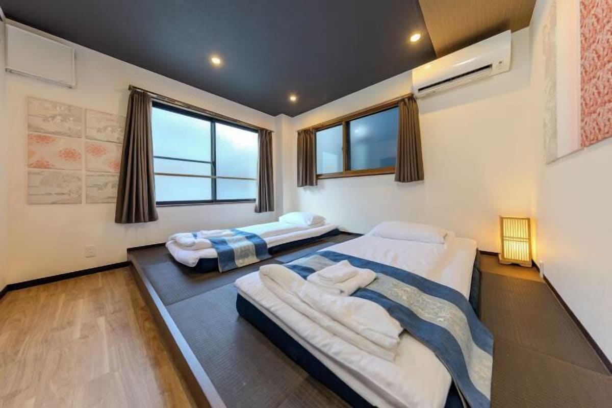 A hotel room with two beds, a large window, and a wall-mounted air conditioner.