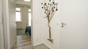 Um corredor com uma decoração de árvore de madeira na parede, uma porta e um vislumbre de um quarto com cama e janela.