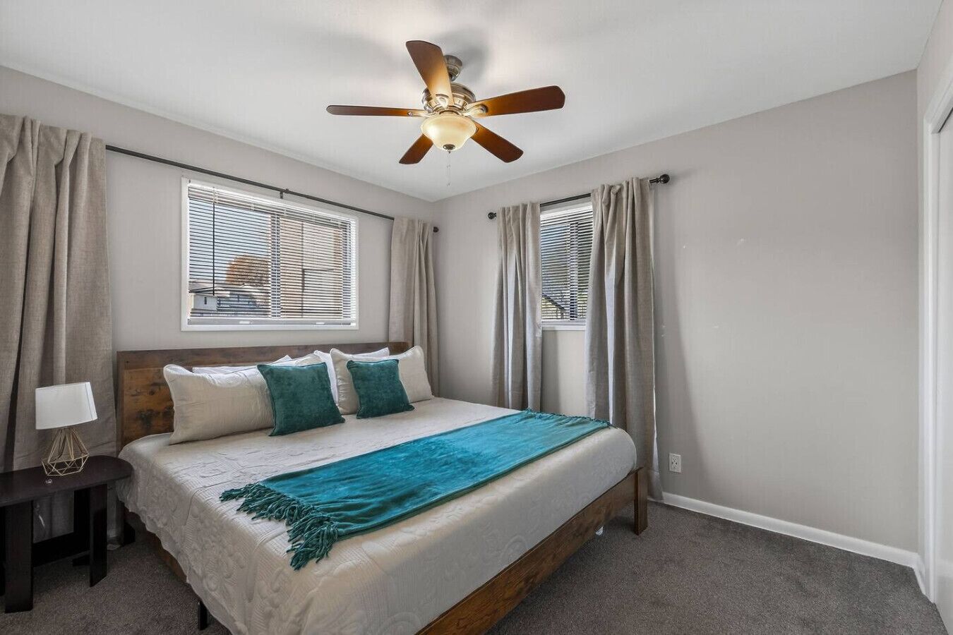A bedroom with a bed, curtains, a ceiling fan, and a window with blinds.