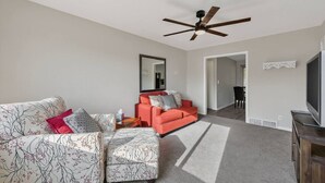 A living room with a sofa, ottoman, and a television. - King Bed 2BR Retreat, Private Garage (Kansas City)